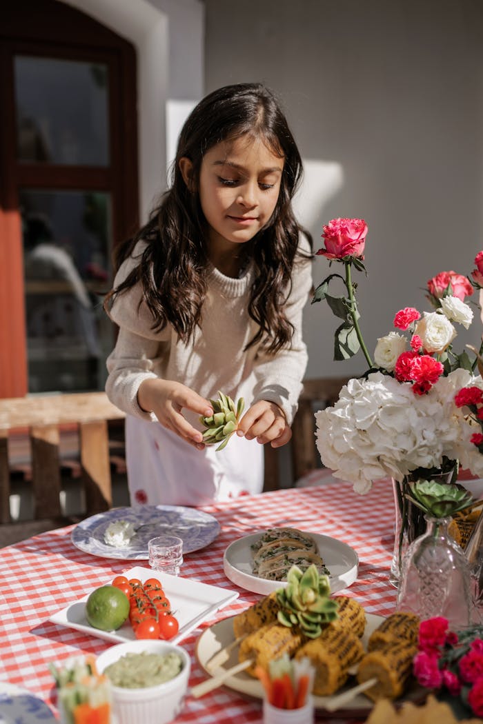 Hispanic girl arranging food for a festive celebration outdoors with flowers and traditional dishes.